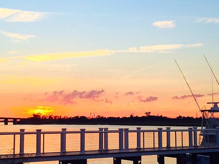 Sunset across the bay from a dock railing in Point Lookout, NY, with a fishing boat's outriggers at right