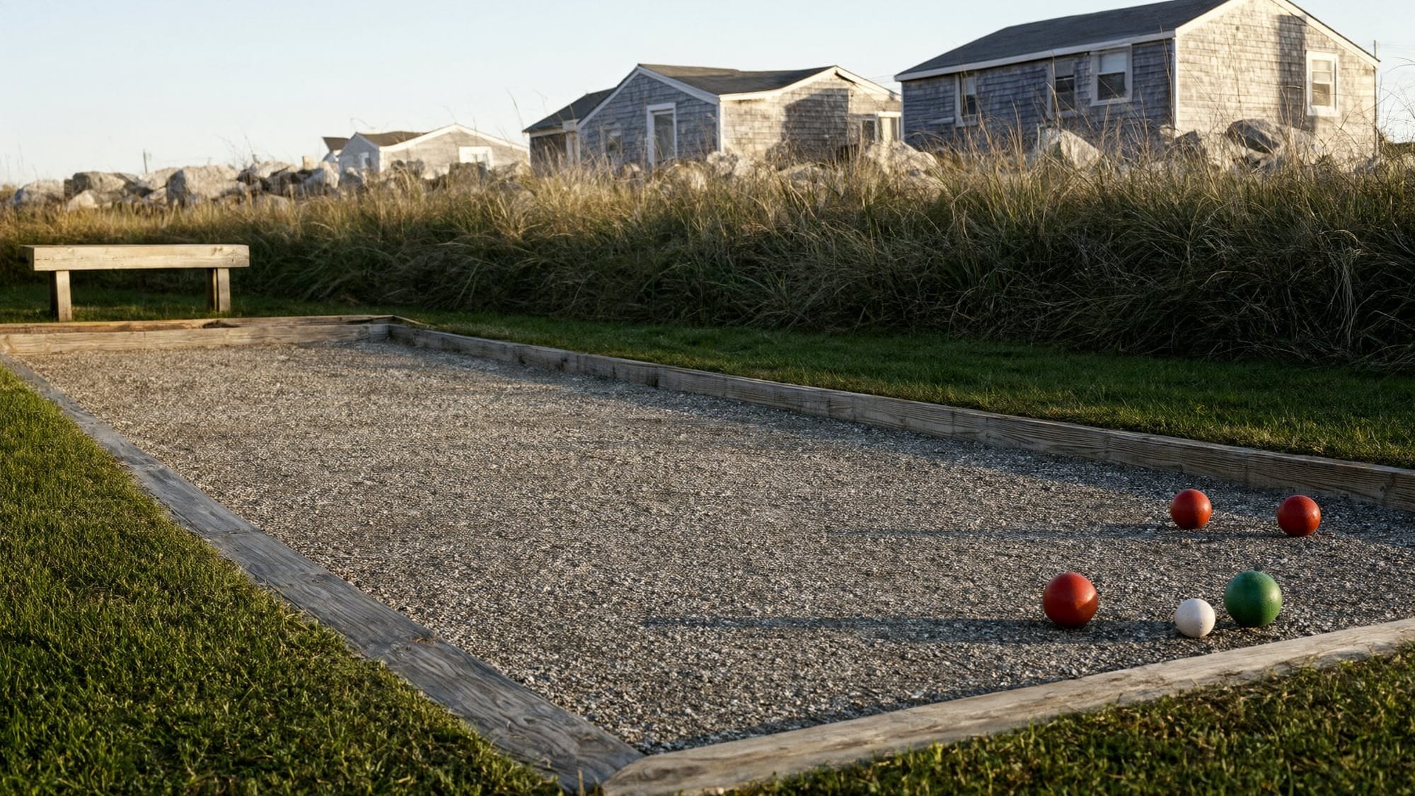 Illustration: a crushed-stone bocce court with red and green balls beside dune grass and gray shingle cottages at golden hour